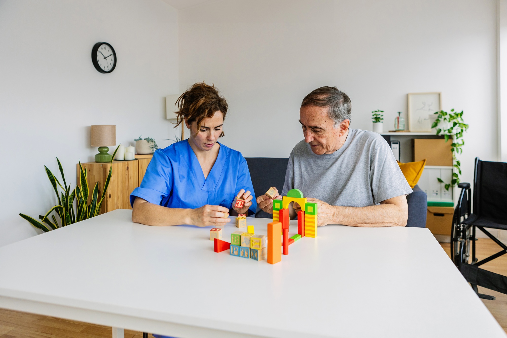 Caregiver and senior man playing wooden shape puzzles for dementia prevention