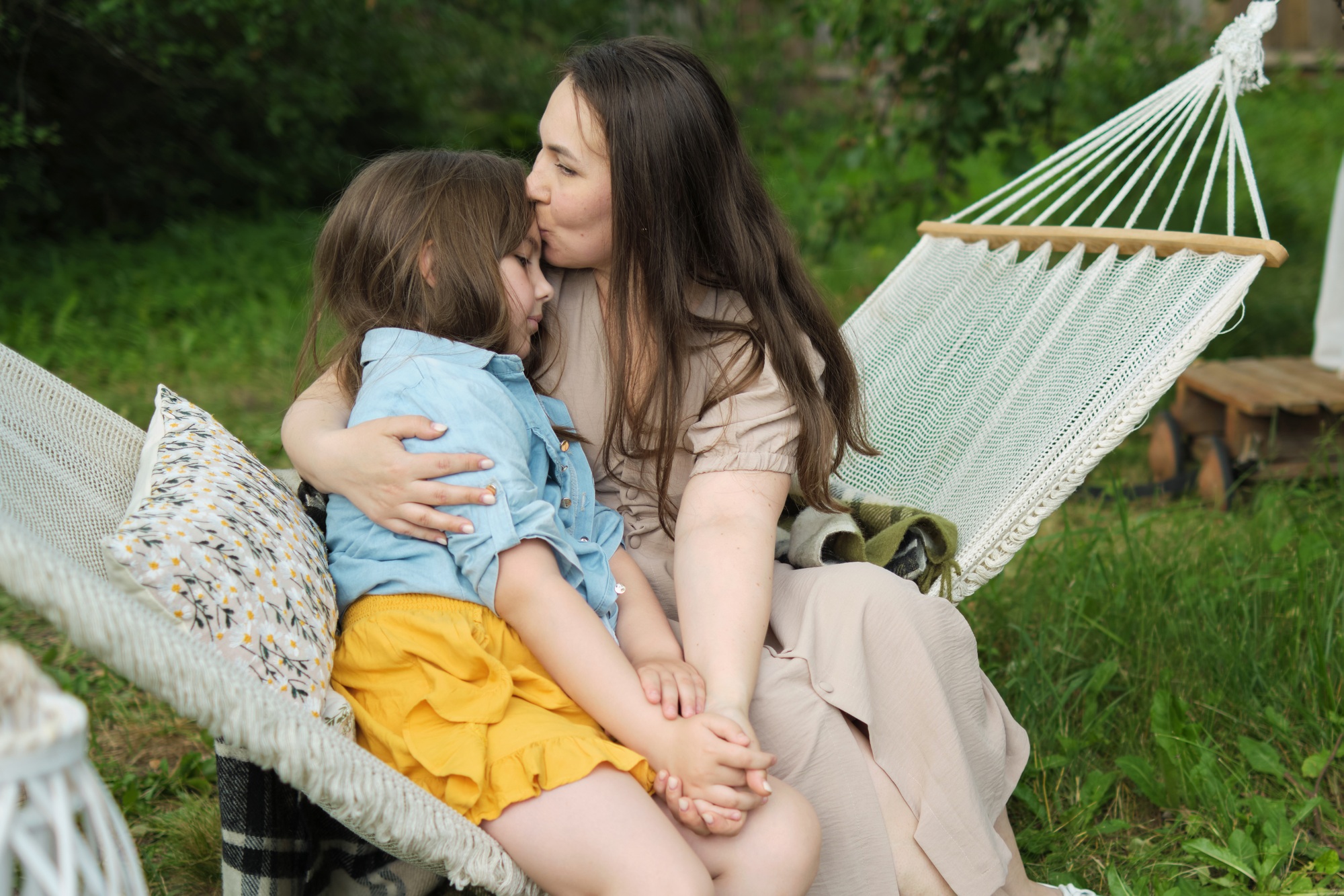 Wrapped in a hammock, a mother affectionately kisses her daughter s forehead, their joyful faces